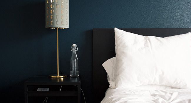 A bed with white pillows, night stand and lamp